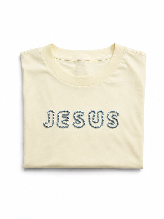 Folded oversized Butter Yellow t-shirt with hand-beaded JESUS lettering