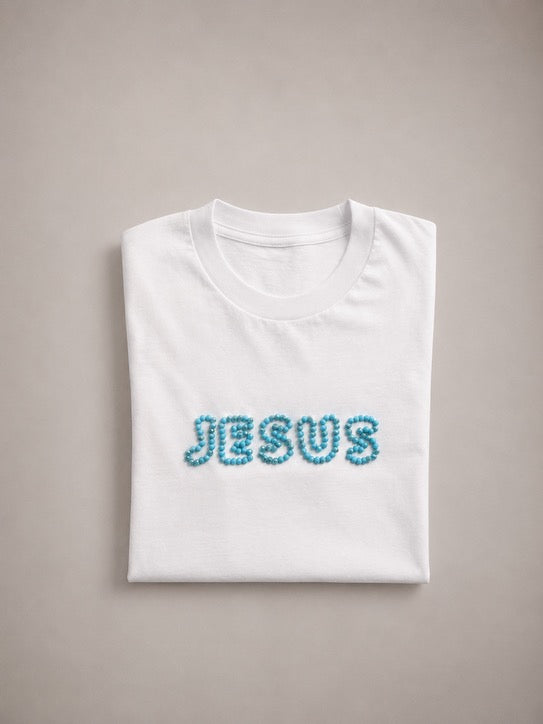 Folded White t-shirt with hand-beaded aqua blue JESUS lettering